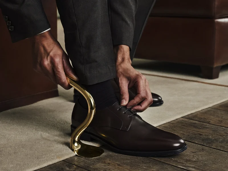 Mani che provano una scarpa in pelle con un calzascarpe in ottone